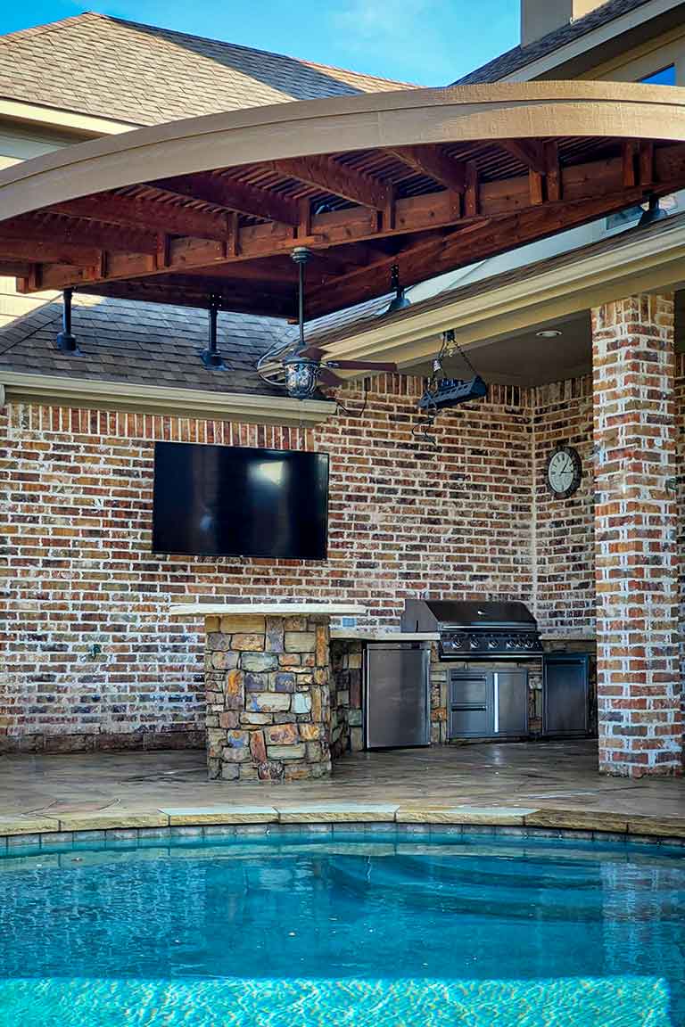 Poolside outdoor kitchen with cedar pergola, stone bar island, and stainless steel grill